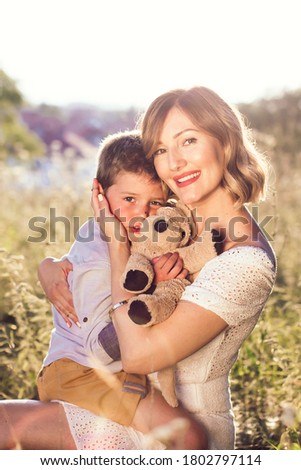 Beautiful young mom holding her blond son in her arms. Outdoor photo. Mothers day