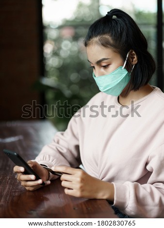Young beautiful woman wears face mask to prevent COVID-19 while chill out and make payment through credit card and smart phone in cafe. Stock photo