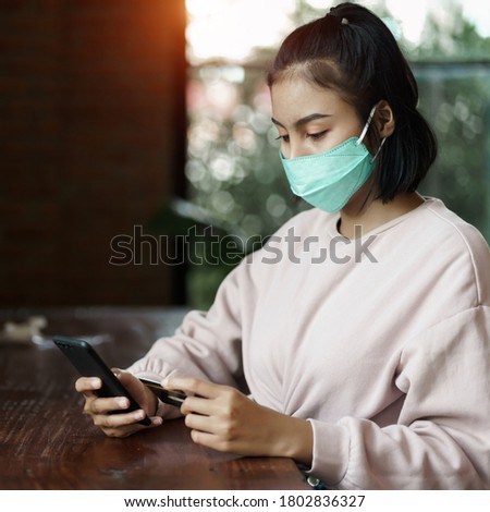 Young teenager woman wears face mask to prevent COVID-19 while chill out and make payment through credit card and phone in the cafe. Stock photo