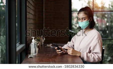 Young teenager woman wears face mask to prevent COVID-19 while chill out and make payment through credit card and phone in the cafe. Stock photo