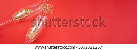 Champagne glass with colorful sugar sprinkles on red background. Holiday, party and celebration concept. Creative flat lay with copy space.