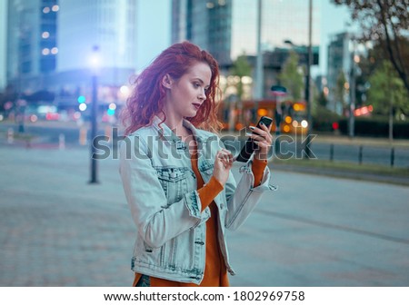 Young Caucasian woman texting cell phone in city at night