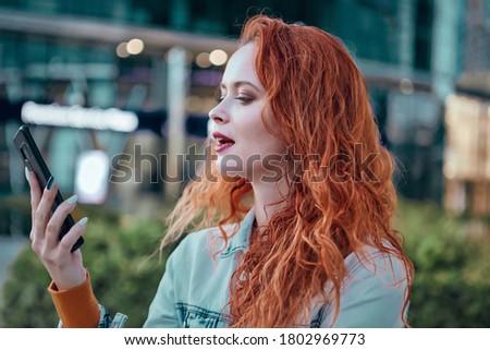 young redhaired woman  standing at night with phone by european skyline
