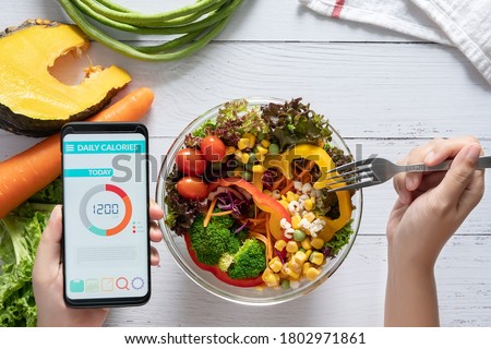 Calories counting , diet , food control and weight loss concept. Calorie counter application on smartphone screen at dining table with salad, fruit juice, bread and fresh vegetable. healthy eating Royalty-Free Stock Photo #1802971861