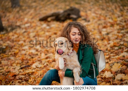 Curly caucasian woman Portrait hugging her golden retriever dog in summer park. Green color background. Young curly woman sitting with her dog outdoors