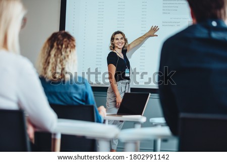 Businesswoman delivering a presentation while pointing at screen looking at colleagues and smiling. Female executive giving an informative presentation to her team during a conference.