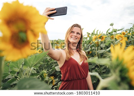 Young Caucasian woman smiling while taking selfie picture with mobile phone in sunflower field. High quality photo