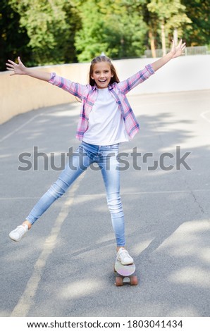 Smiling happy cute little girl child  skating on a skateboard. Preteen riding on a penny board outdoors in summer day