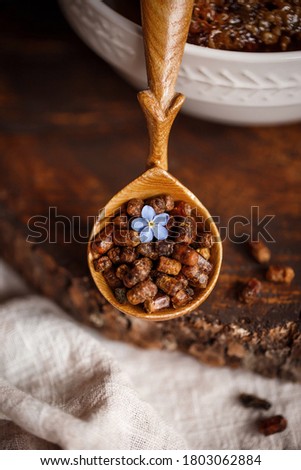 Wooden brown spoon close up with bee products with Perga bee parchment next to honey in combs on a wooden brown cut on a linen cloth tablecloth with blue flowers and one flower on top of parchment
