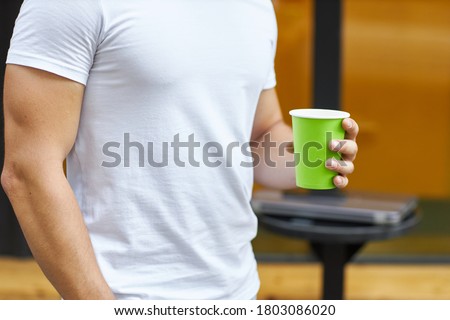 Young man standing in the street with coffee in his hands. Shallow depth of field with focus on it. Place to write