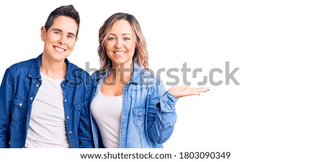 Couple of women wearing casual clothes smiling cheerful presenting and pointing with palm of hand looking at the camera. 