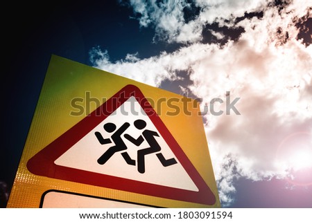 Road sign: Caution, children. The sign is photographed against a cloudy daytime sky.