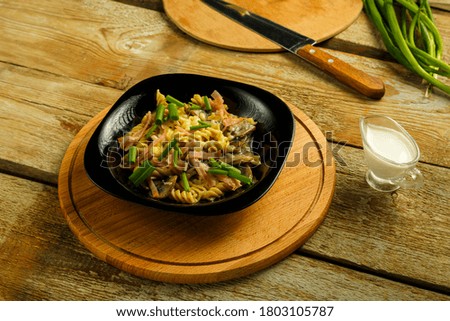 Black plate with pasta with ham and mushrooms in a creamy sauce on the table with a fork in the background.