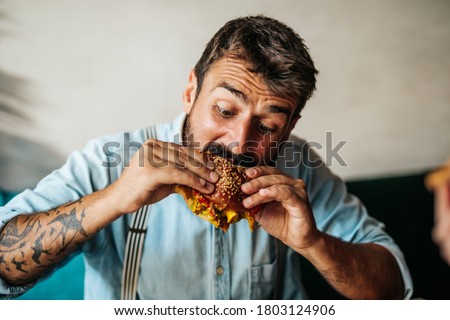 Handsome middle age man sitting in restaurant and enjoying in delicious burger.  Royalty-Free Stock Photo #1803124906