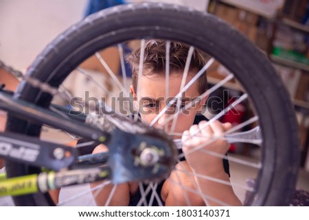 A little boy is sitting in the garage and fixing a wheel on his bike