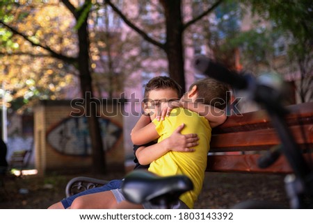Two embracing boys are sitting on a park bench