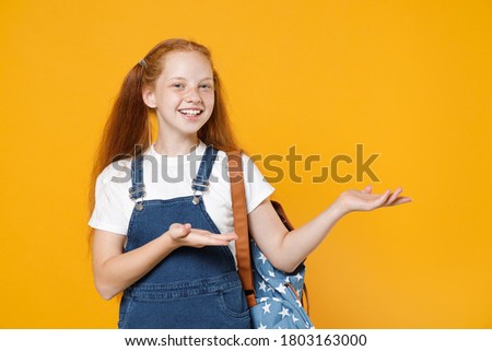 Young school teen kid girl 12-13 years old in white tshirt blue uniform backpack pointing fingers hands on workspace isolated on yellow background children studio portrait education lifestyle concept