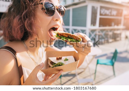 Happy woman eats a fast food flatbread with filling sitting on the street and resting after a working day. Concept of healthy food and extra calories