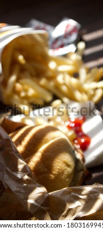 Blur picture of burger and fries with ketchup on white tissue paper under shade of natural light