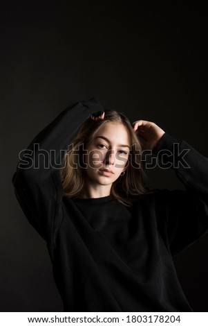 brunette teen girl dressed in black runs her hands through her hair, black background
