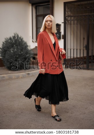 Young woman model in a red jacket and black dress on the street, fashion photography, street style.