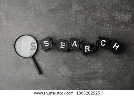 Word SEARCH made of black cubes and magnifier glass on grey stone background, flat lay. Find keywords concept