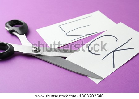 Cut paper with word LUCK and scissors on purple background, closeup
