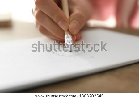 Woman correcting picture in notepad with pencil eraser at table, closeup