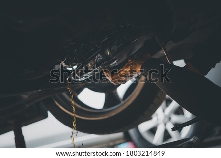 Car mechanic drain the old automatic transmission fluid (ATF) or gear oil at car garage for changing the oil in a gear box of car engine Royalty-Free Stock Photo #1803214849