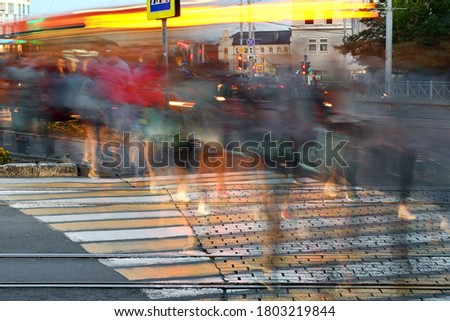 People move along the crossing in the evening. Their image is blurry. Legs are in focus