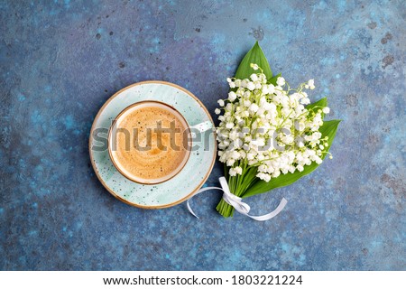Lily of the valley flowers bouquet and coffee cup on blue background. Breakfast, morning coffee, greeting card concept. Top view, flat lay
