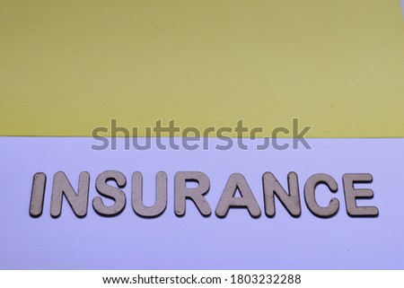 The word says INSURANCE written in 3d wooden alphabet letters laid on a pair of solid color foam sheet background. Property protection concept, selective focus.