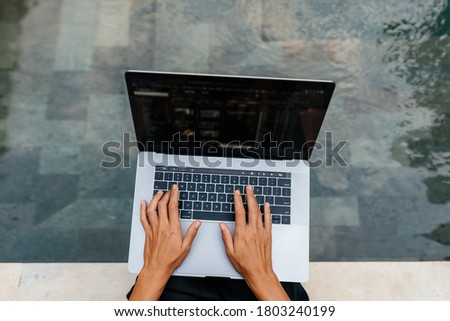 Woman working on her laptop computer sitting at poolside.