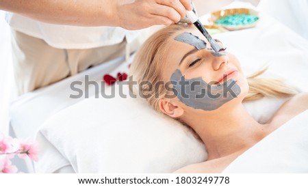 Skin face care and Beauty treatment concept.Beautiful young attractive Caucasian woman masking face with natural clay for skin care and having massage by Thai Masseuse in aroma spa salon.