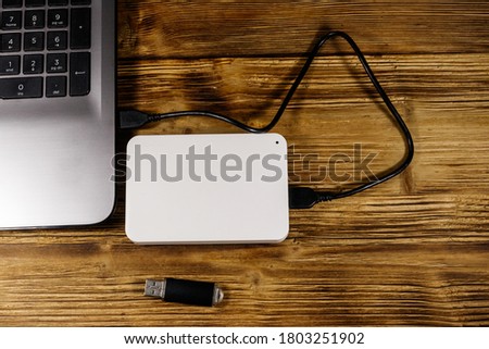 External HDD connected to laptop computer and USB flash drive on a wooden desk. Top view. Concept of data storage