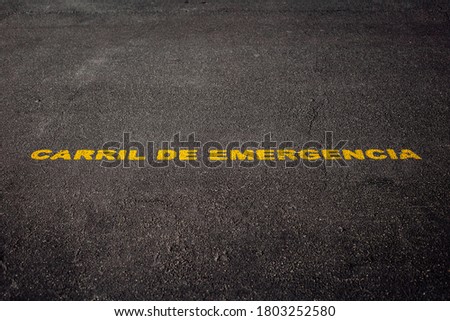 Yellow warning sign written on a black asphalt floor. Emergency lane in spanish on a urban road. City details.