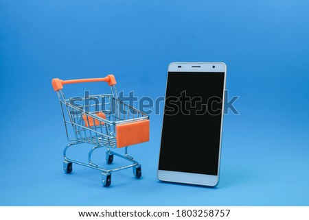 A smartphone and a supermarket trolley on blue background 
