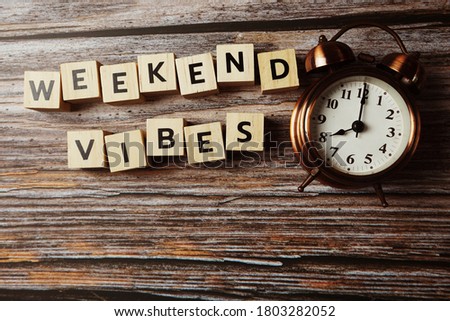 Weekend Vibes alphabet letter with alarm clock on wooden background;
