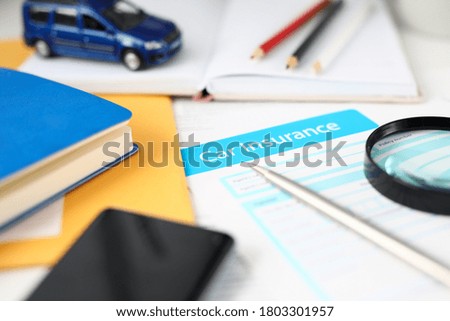 Close-up of signing important documents about car insurance of clients. Blue model of vehicle, pencils, notebook, smartphone and magnifier on table. Assurance concept