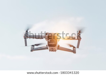 Drone with digital camera flying on sunny sky. Modern RC quadcopter.