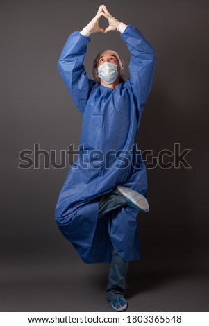 The doctor dances on a gray background, an empty space for text. The doctor is happy, he is having fun. A man in a blue robe, hat, gloves, in a medical mask.