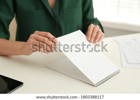 Woman with pencil and notepad at white table, closeup