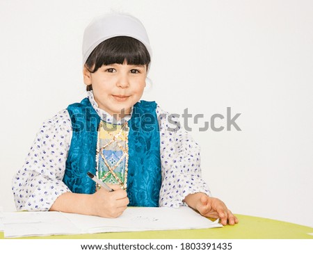 A little girl is sitting at a table, doing a drawing task, smiling and looking at the camera