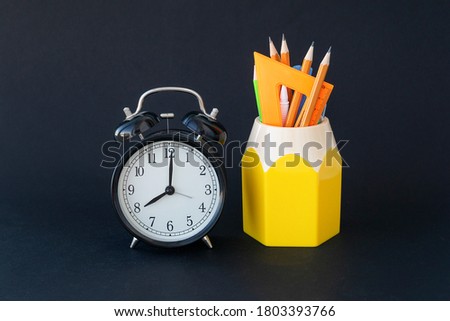 back to school concept. School supplies and round clock are on black background. Copy space for text. Beginning of school year, time for study