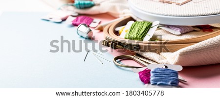 Embroidery set fot cross stitching. White fabric, embroidery hoop, colorful threads, scissors and needls. On blue background. Hobbies concept with copy space, banner. Royalty-Free Stock Photo #1803405778