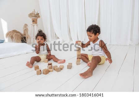 Little Brother and Sister  African American play houses with wooden eco bricks, build and destroy towers. Fine motor development, educational games. White interior in background with wooden floor