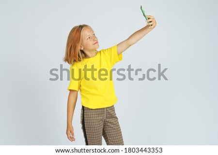 A teenage girl in a yellow T-shirt takes a selfie on a mobile phone. Isolated background. Education concept.