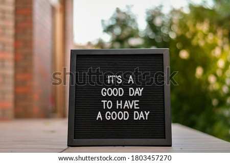 "Its a good day to have a good day" words written on a black letterbox on the outdoor terace. Blurred background.