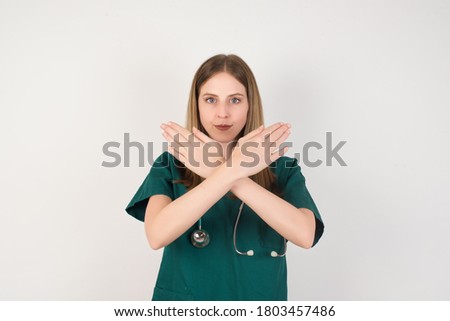 Female doctor wearing a green scrubs and stethoscope is on white background has rejection expression crossing arms and palms doing negative sign, angry face.
