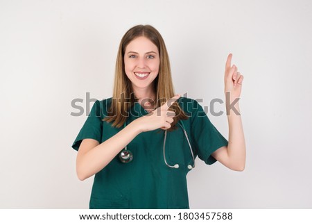 Female doctor wearing a green scrubs and stethoscope is on white background indicating with forefinger empty space showing best low prices 